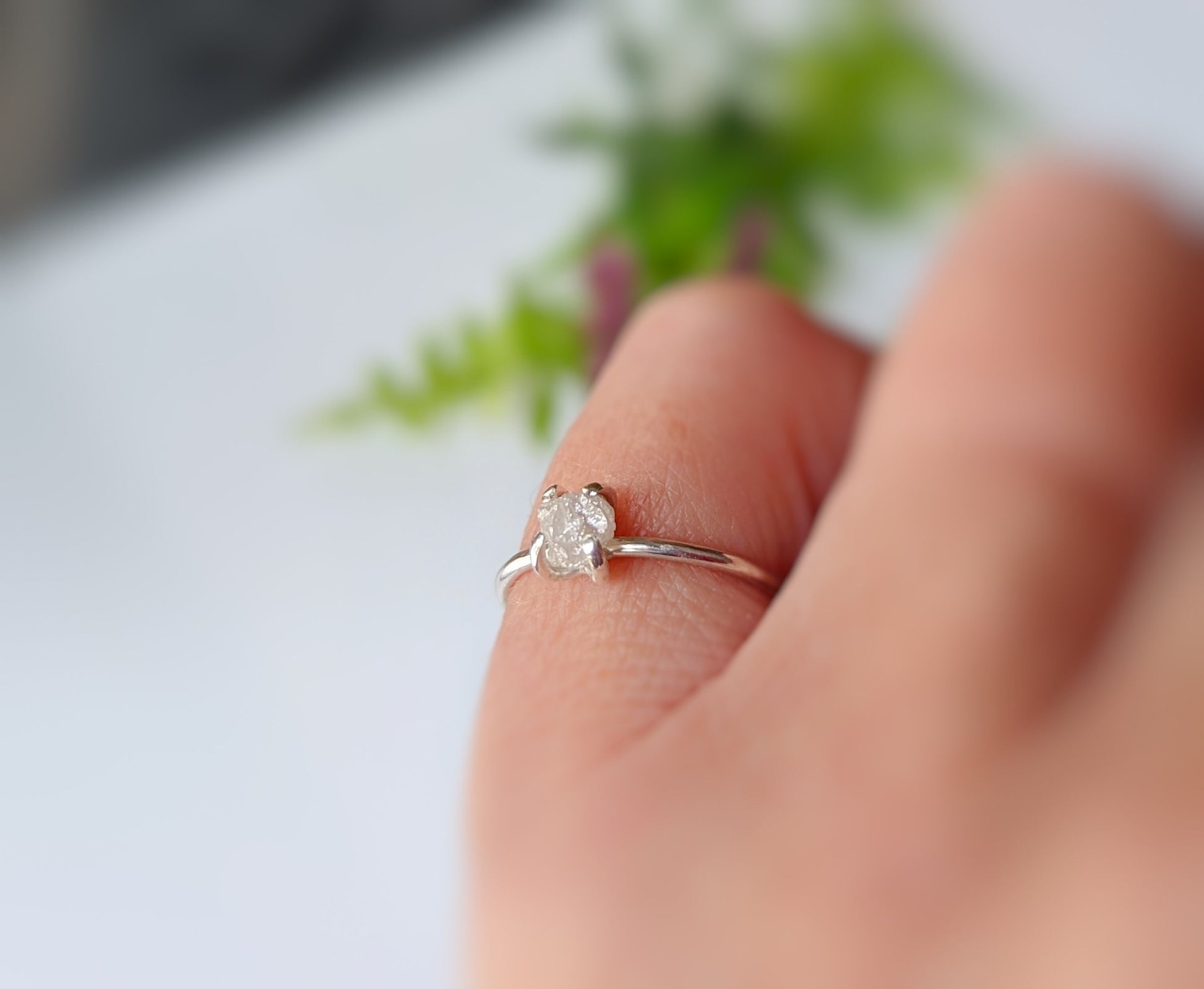Hand wearing a delicate sterling silver raw diamond engagement ring with a sparkling center stone.