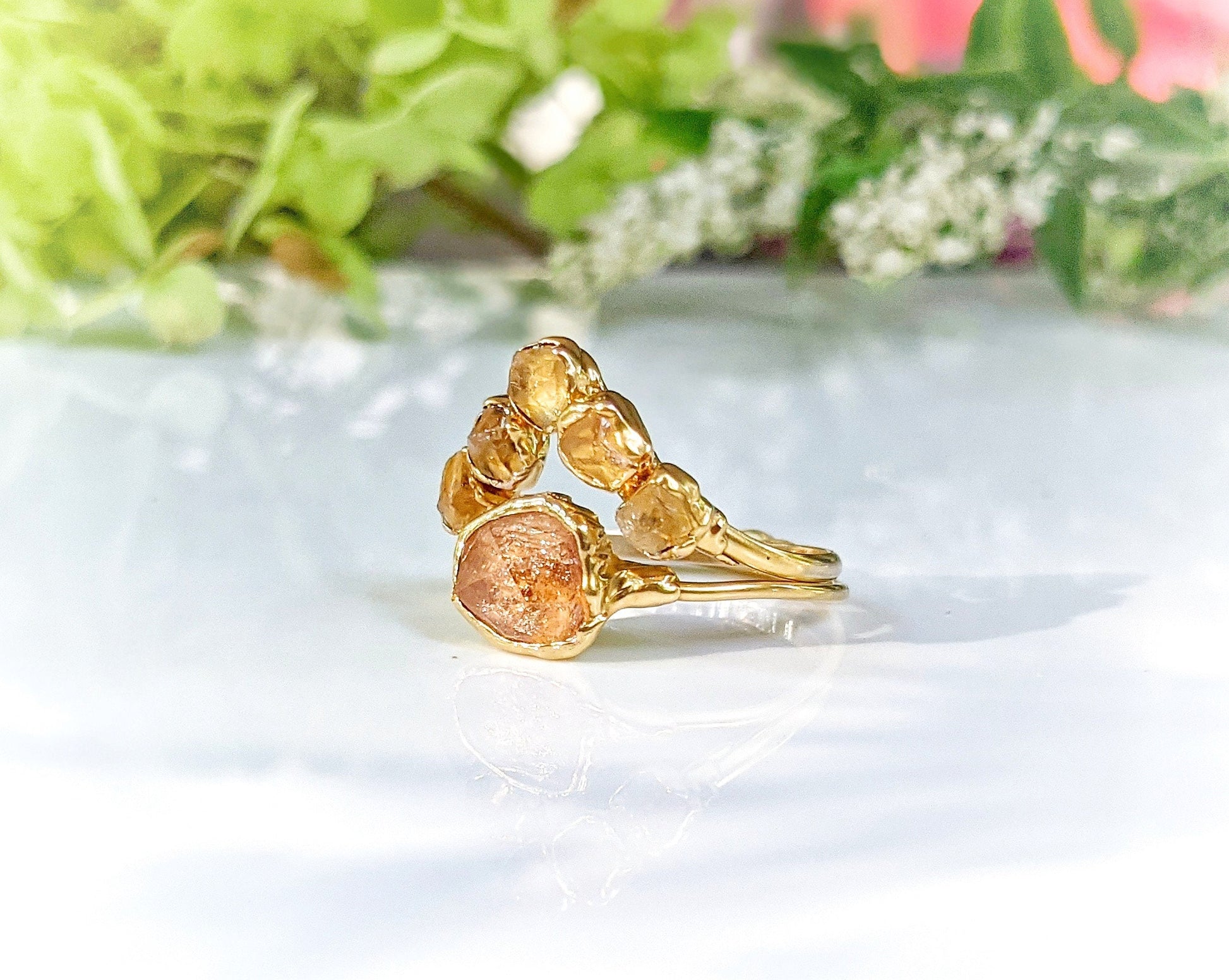 Raw Topaz and Citrine Chevron ring set on a reflective surface, showcasing unique gemstones in a gold setting.
