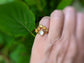 Raw Citrine and Herkimer diamond Chevron engagement ring worn on a hand among green leaves.