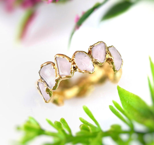 Rose Quartz eternity gold ring with irregular gemstones on a gold-filled band, set against lush greenery.