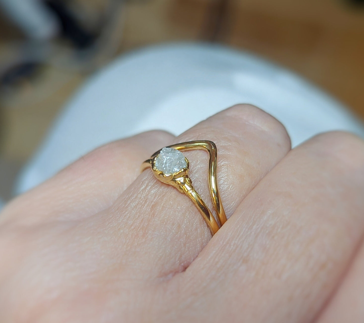 Raw diamond engagement ring set on a hand, featuring a unique uncut diamond and 18k gold chevron band.