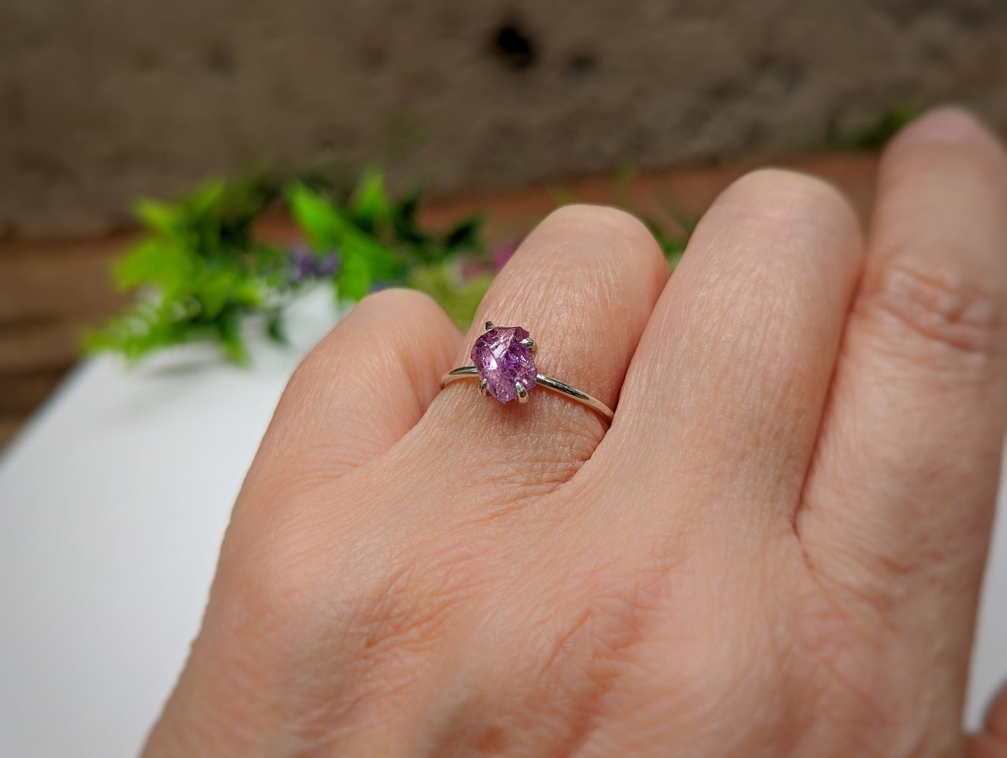 Handcrafted raw Alexandrite ring set in sterling silver, showcasing unique sparkle on a hand with greenery in background.