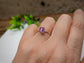 Handcrafted raw Alexandrite ring set in sterling silver, showcasing unique sparkle on a hand with greenery in background.