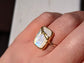 Close-up of a handmade Moonstone Kintsugi ring on a hand, featuring a gold band and iridescent stone.