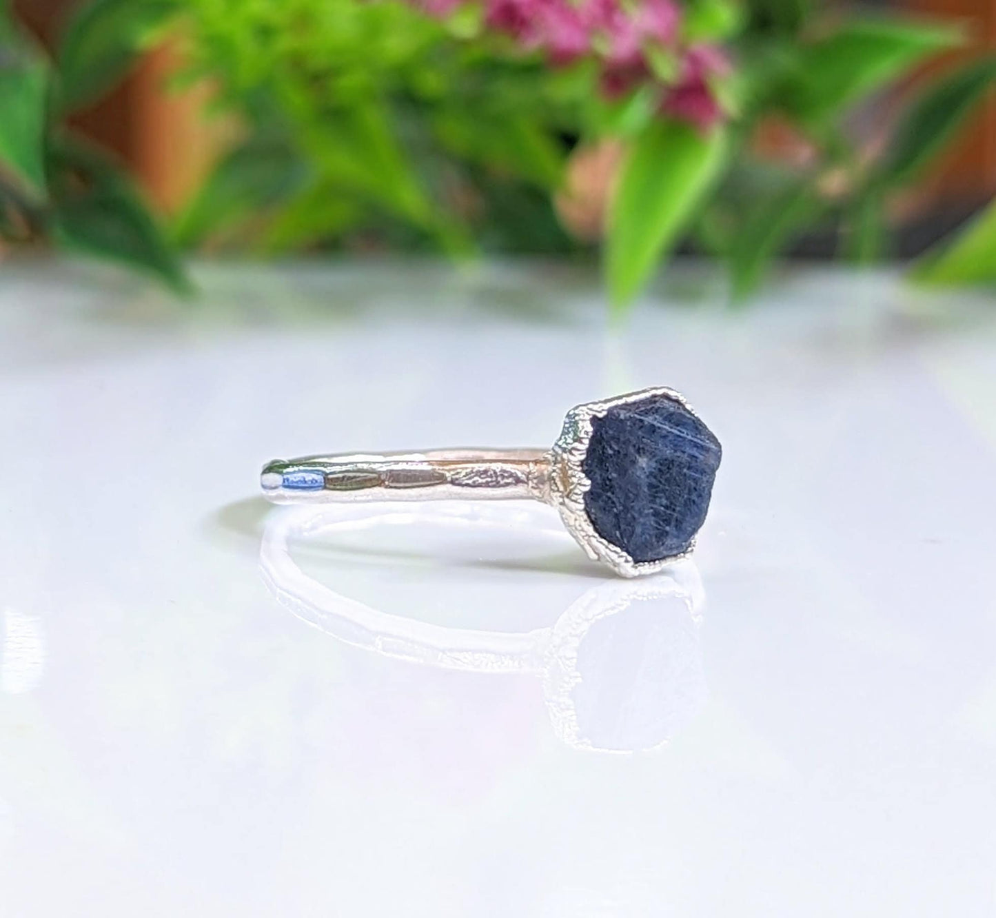 Handcrafted raw sapphire ring on a reflective surface, set in sterling silver with a rustic design.