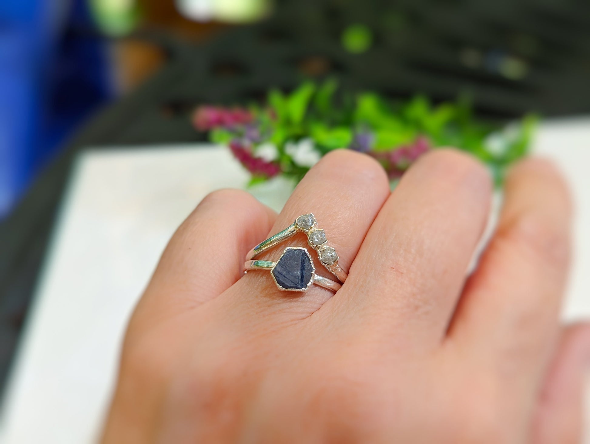 Handcrafted raw blue sapphire ring on a hand, featuring a sterling silver band and delicate stone accents.