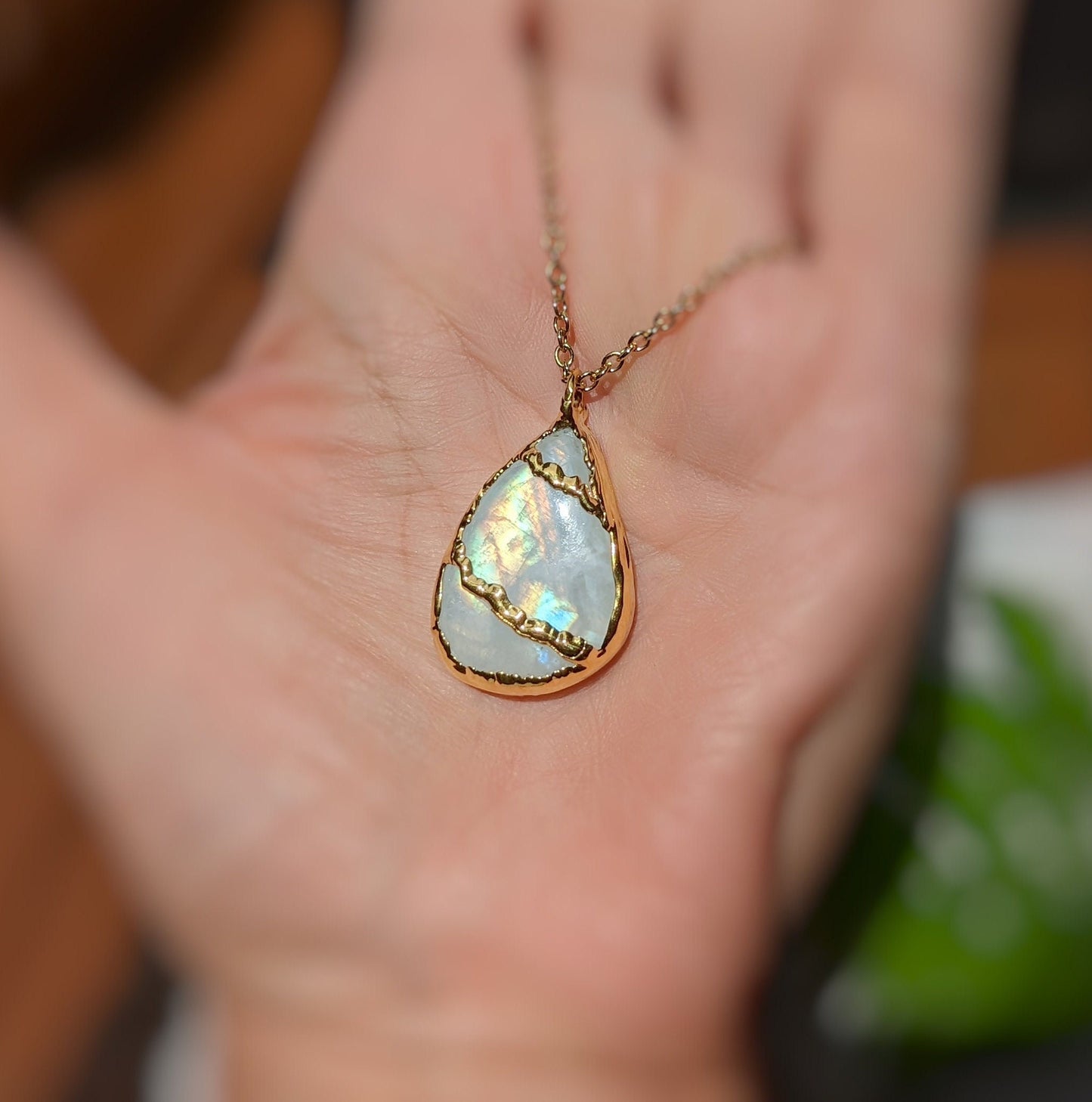 Rainbow Moonstone Kintsugi necklace on a hand, featuring electroformed design and gold plating.