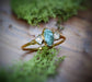 Raw green Sapphire and diamond engagement ring on a wooden surface, surrounded by green moss, handcrafted in 14k gold.
