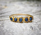 Raw sapphire multi-stone eternity ring on a textured surface, featuring small blue sapphires in a 14k gold filled band.