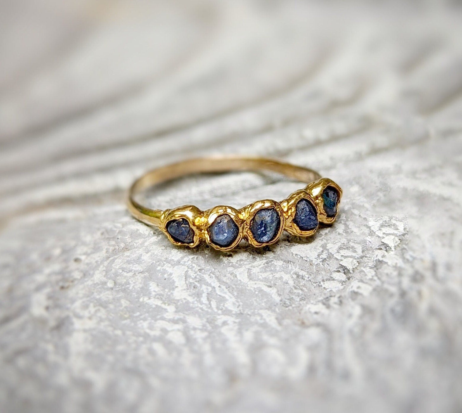 Raw sapphire multi-stone ring on a textured surface, featuring small blue sapphires set in a solid gold band.