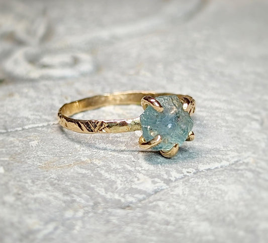 Teal-blue raw Montana Sapphire engagement ring with textured gold band, symbolizing natural elegance.