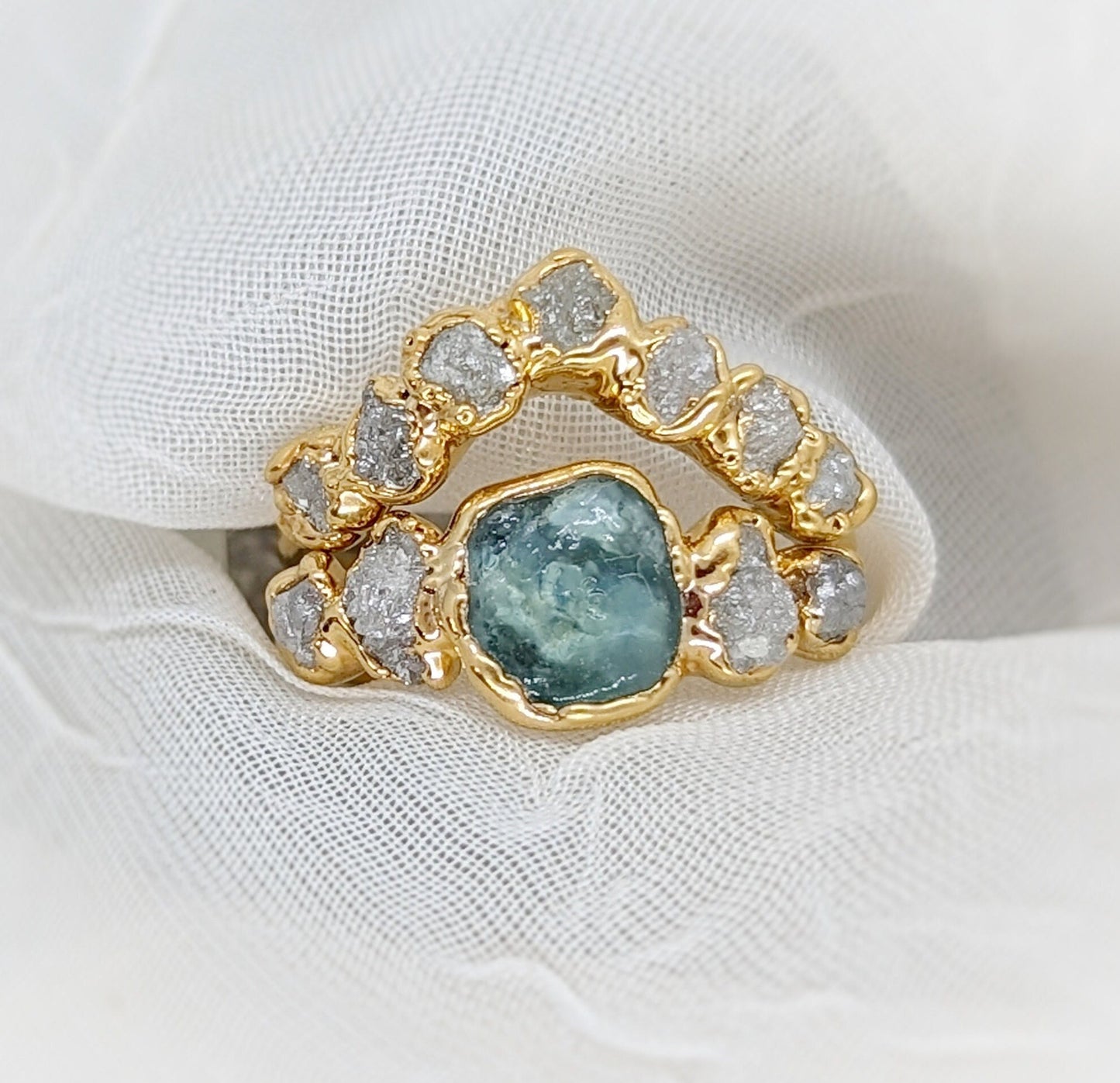 Raw Montana Sapphire and diamond ring set in 14k gold on a soft fabric background, symbolizing unique love.