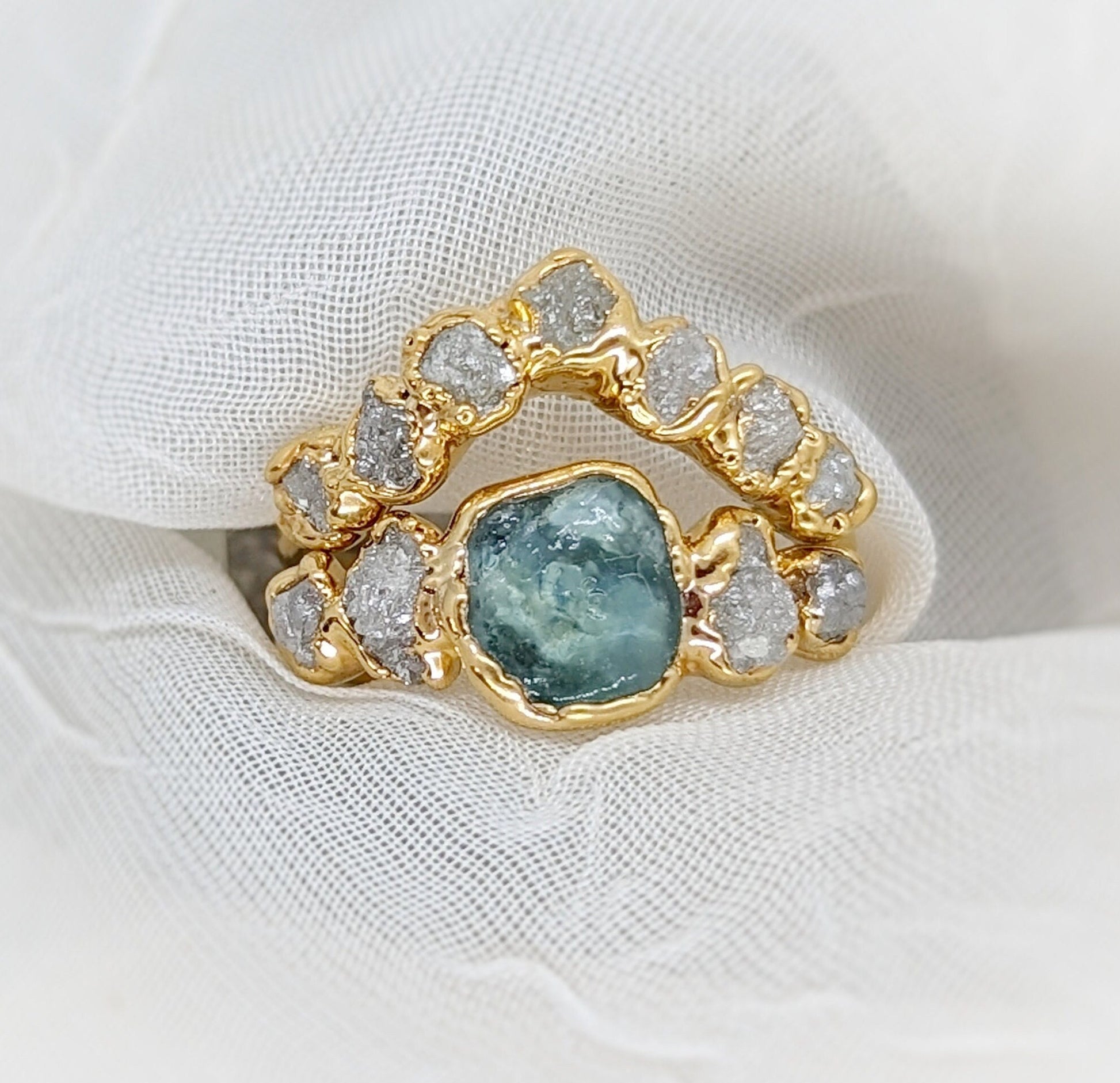 Raw Montana Sapphire and diamond ring set in 14k gold on a soft fabric background, symbolizing unique love.