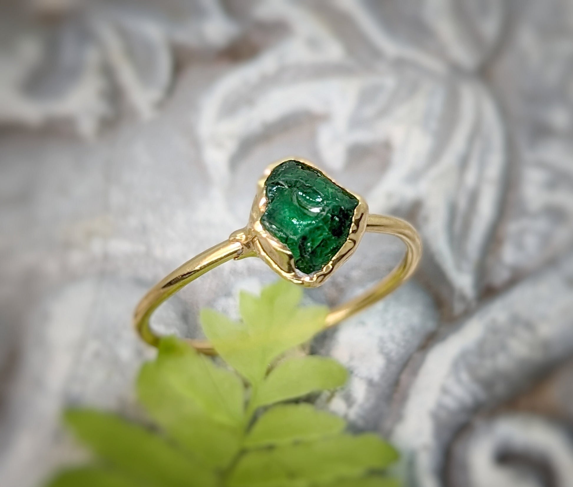 Handcrafted raw green Garnet ring featuring a natural uncut stone set in a gold band, on a textured background.