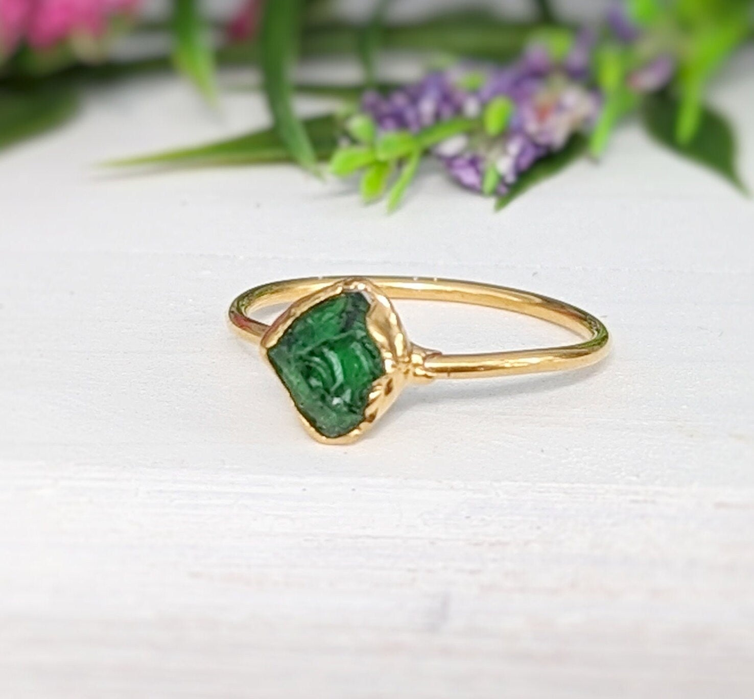 Handcrafted raw green Garnet ring with uncut edges, set in gold, highlighted against a floral background.