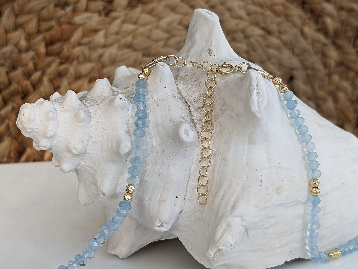 Handmade aquamarine bead necklace with gold accents resting on a seashell, symbolizing calmness and serenity.