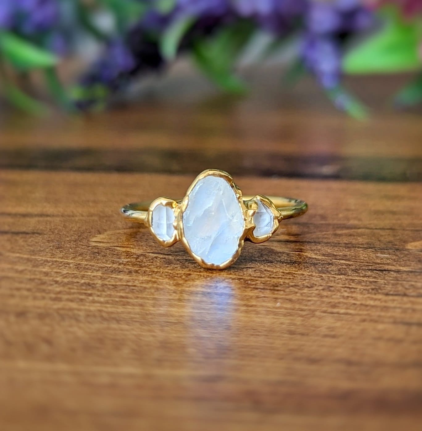 Raw rainbow Moonstone and Herkimer diamond engagement ring on a wooden surface, featuring a gold-filled band.