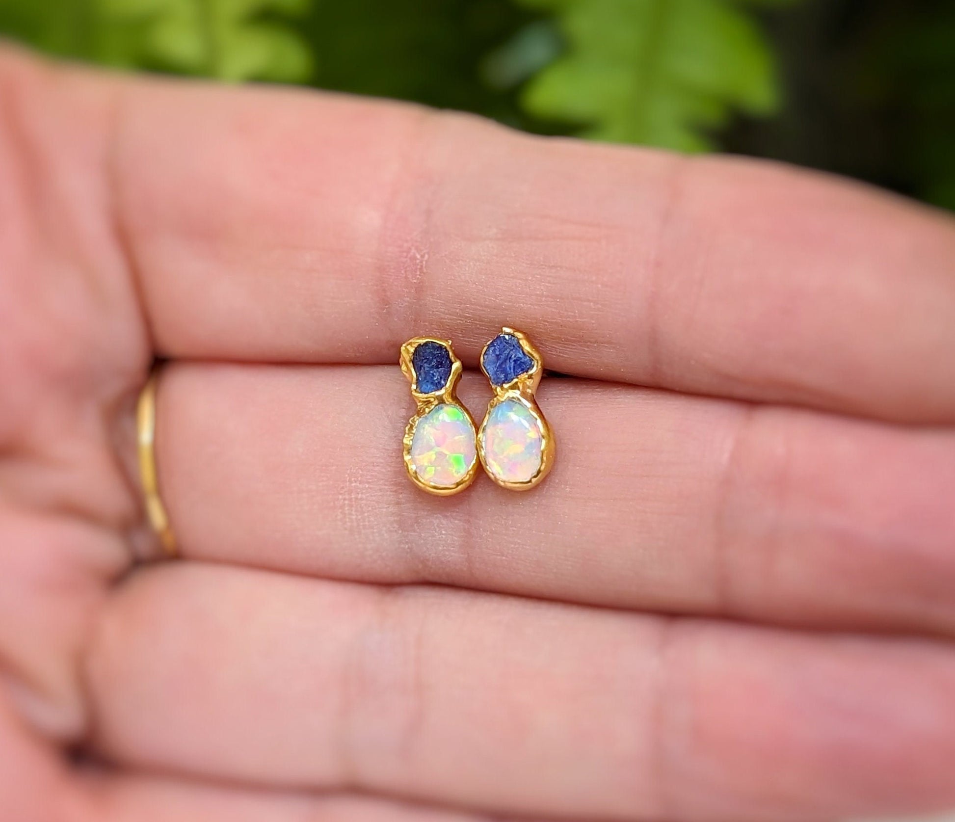 Dainty raw sapphire and opal stud earrings, elegantly handcrafted and held in a hand.