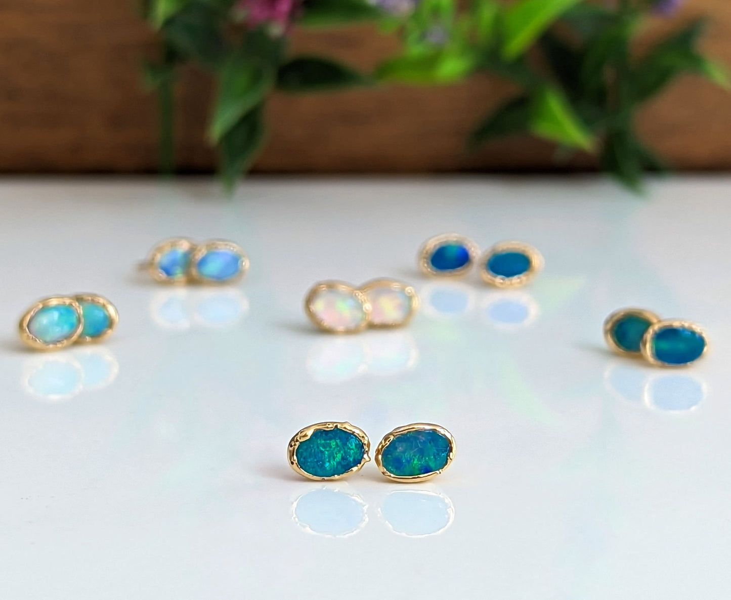 Light blue Australian Opal stud earrings on a reflective surface, showcasing elegance and unique craftsmanship.