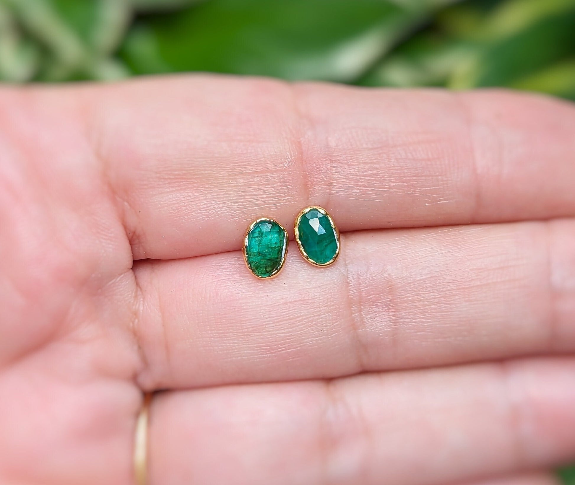 Natural Emerald stud earrings set in 18k Gold, showcasing elegant green gemstones on a hand.