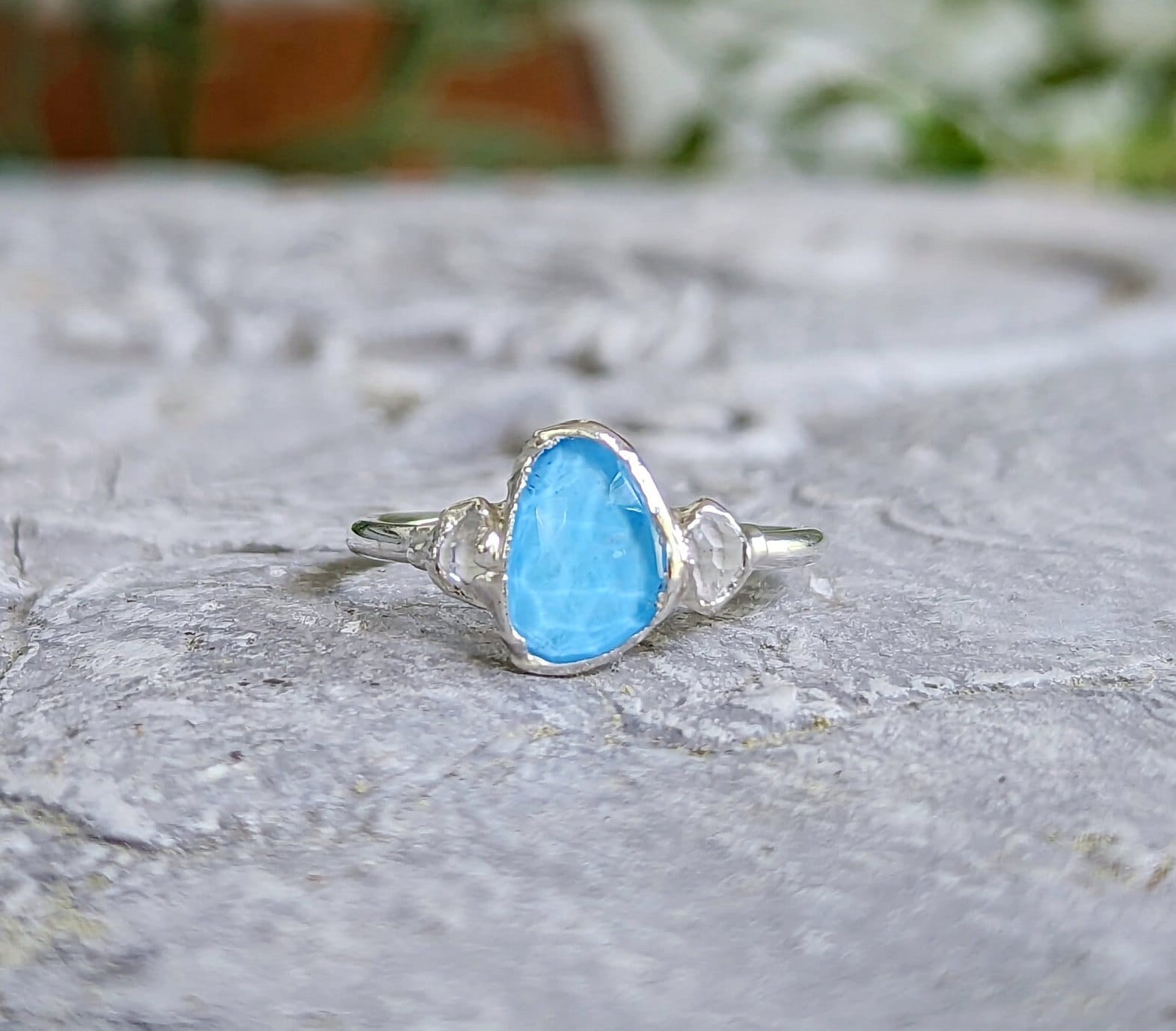 Blue Topaz and Herkimer diamond engagement ring on sterling silver band, showcased on a textured stone surface.