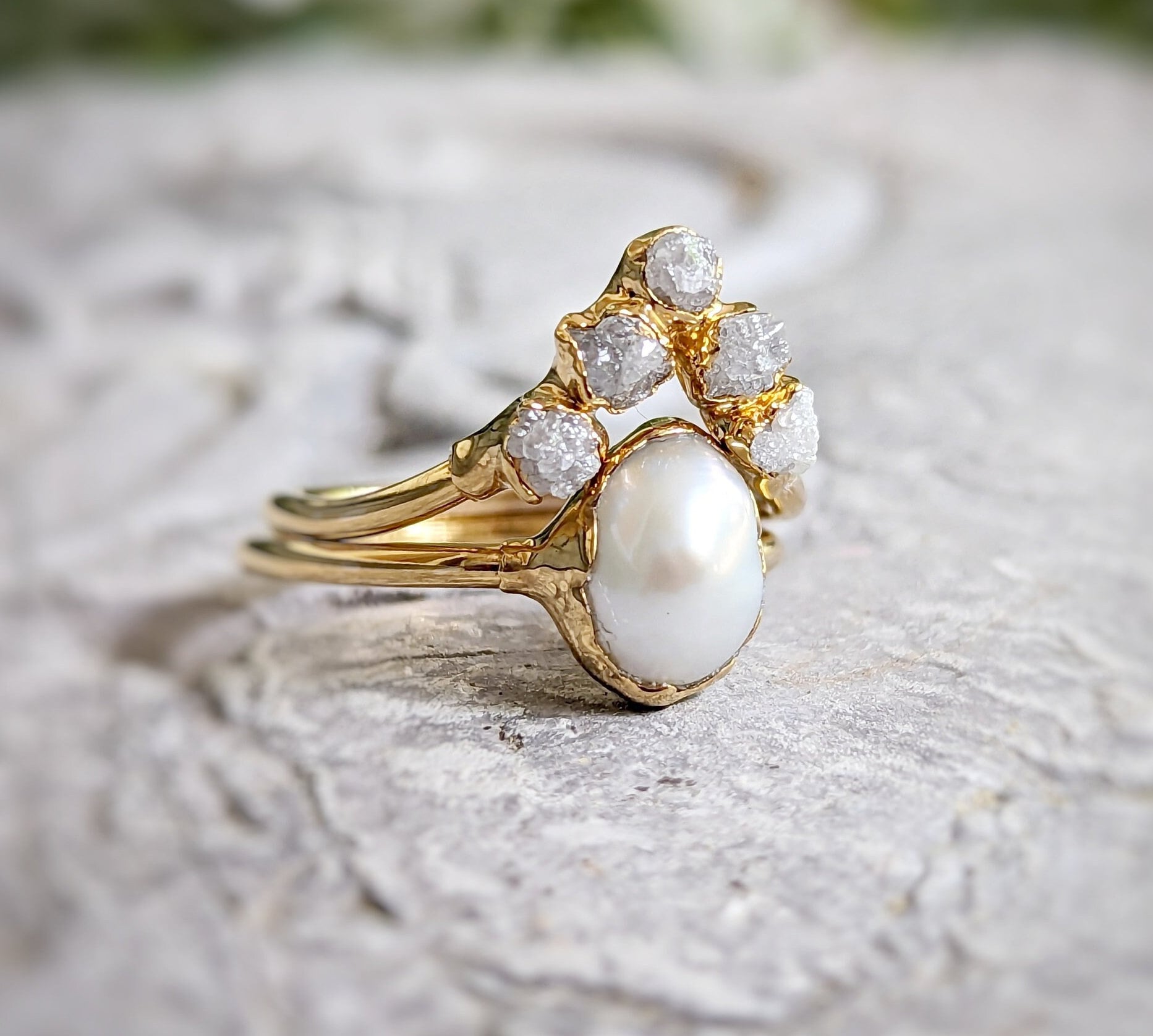 Freshwater pearl and raw diamond chevron wedding ring set in solid 14k gold on textured stone background.
