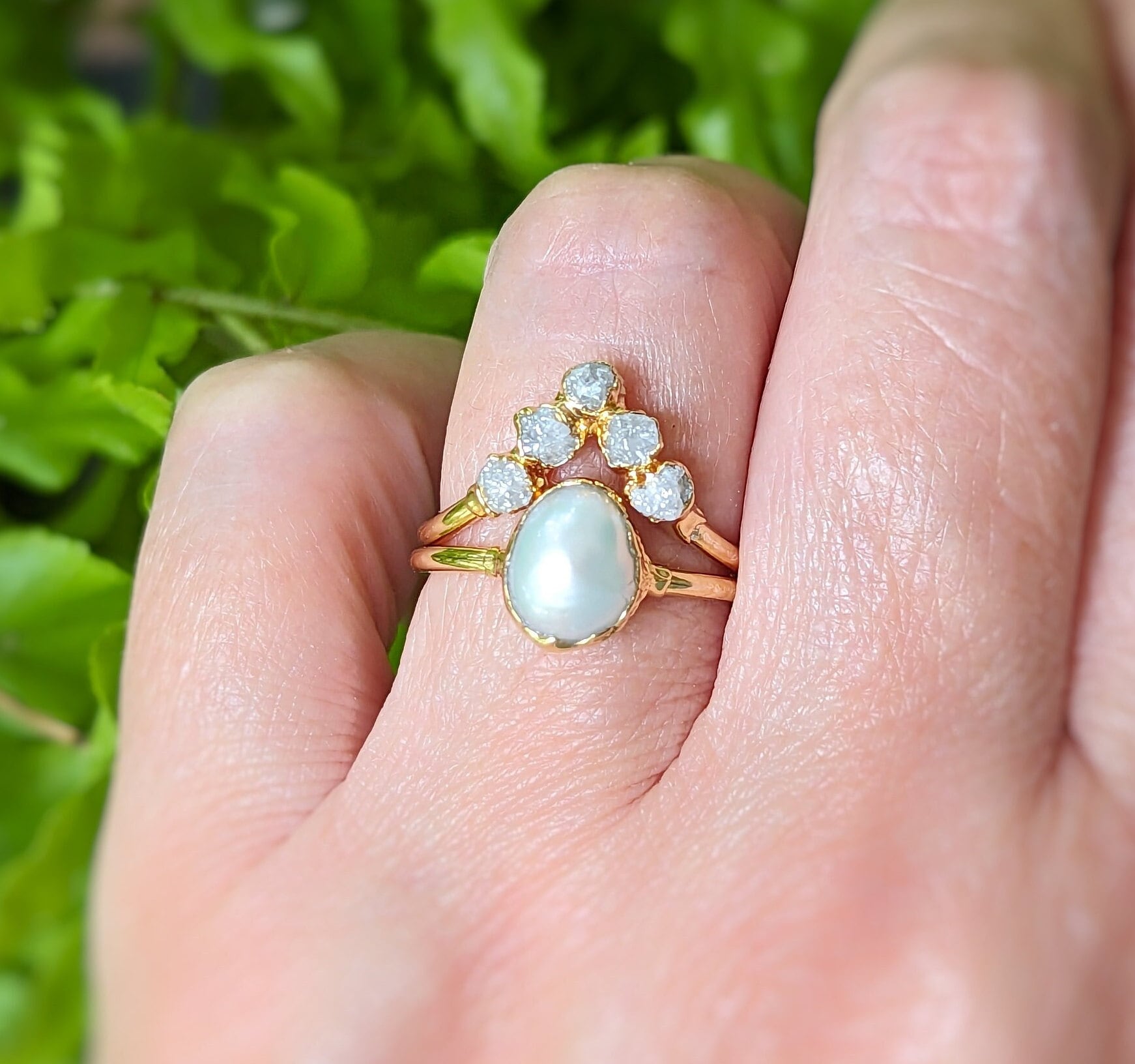 Freshwater pearl and raw diamond chevron wedding ring set in solid 14k gold on hand amidst lush greenery.