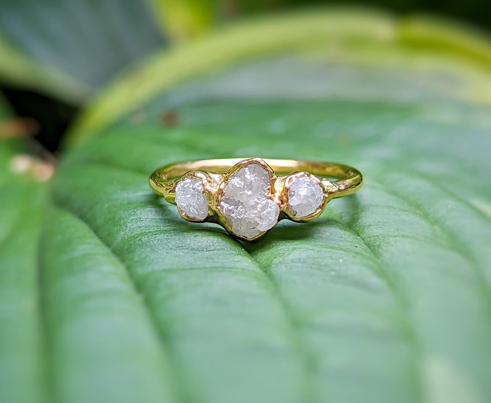 Handcrafted raw multi diamond engagement ring on a green leaf background, featuring uncut diamonds in gold band.