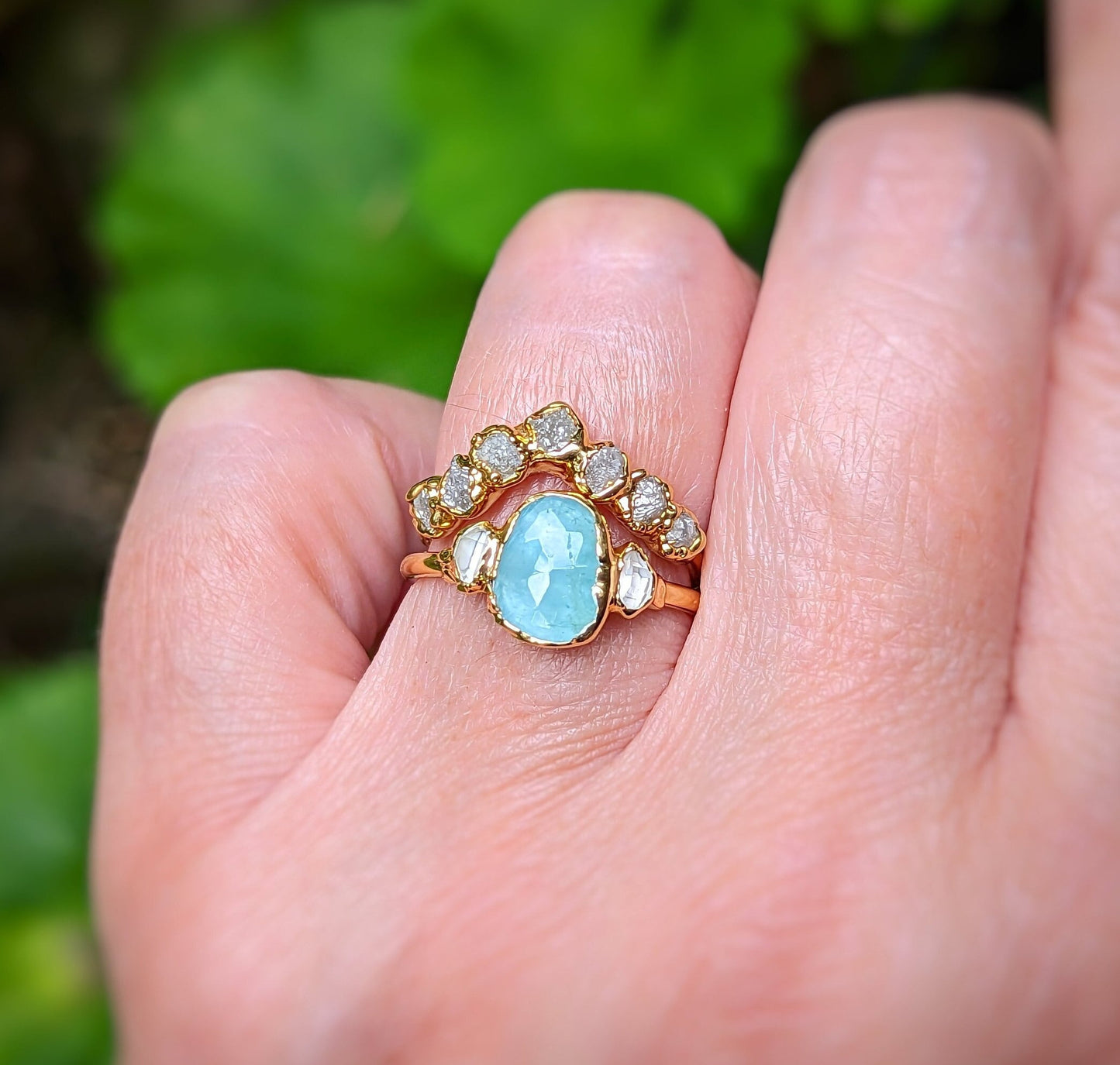 Unique gold Chevron wedding band featuring raw diamonds and an aquamarine stone on a hand outside.