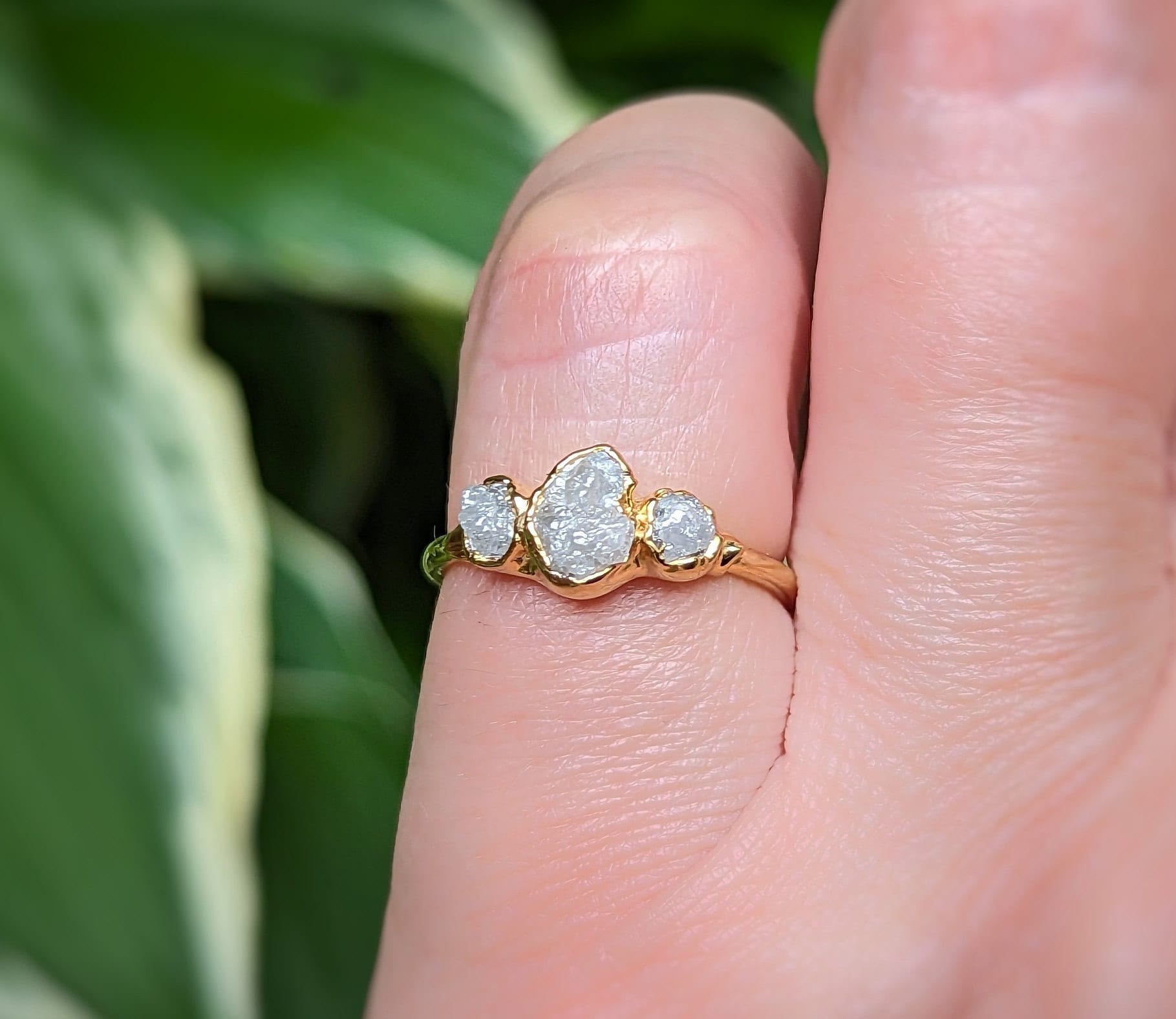 Rustic raw diamond engagement ring on a hand, featuring uncut diamonds on a gold band, perfect for unique proposals.