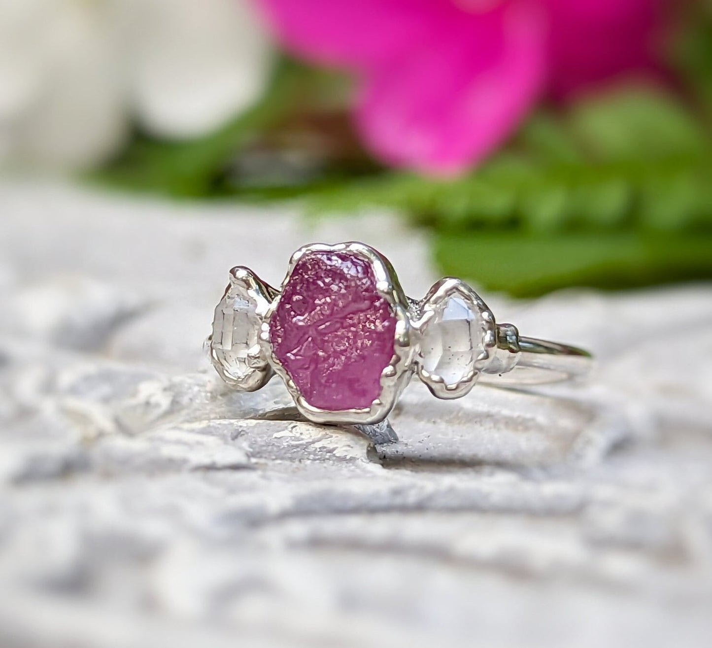 Raw pink sapphire and Herkimer diamond engagement ring on a textured surface, highlighting its unique design.