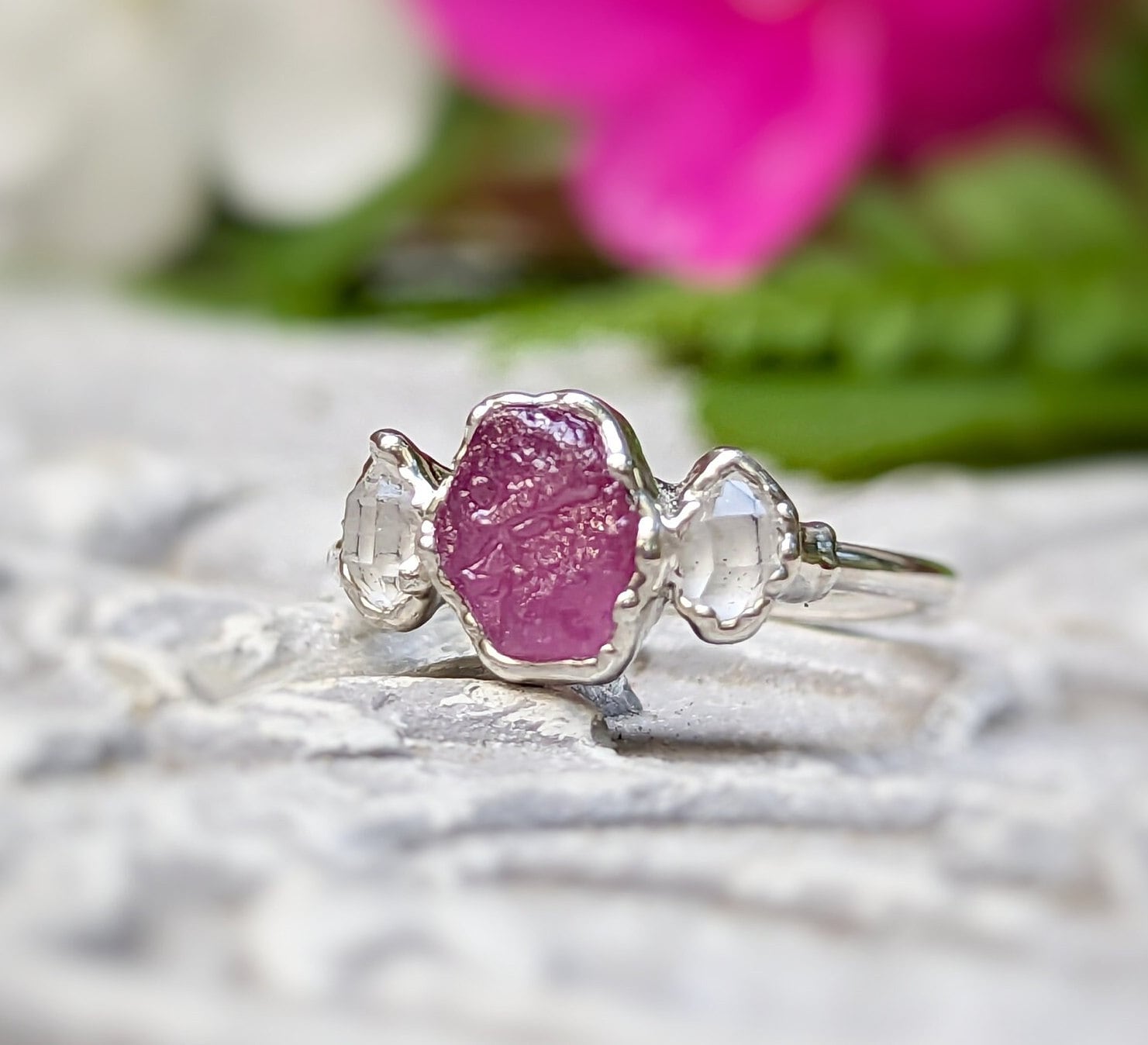 Raw pink sapphire and Herkimer diamond engagement ring on a textured surface, highlighting its unique design.