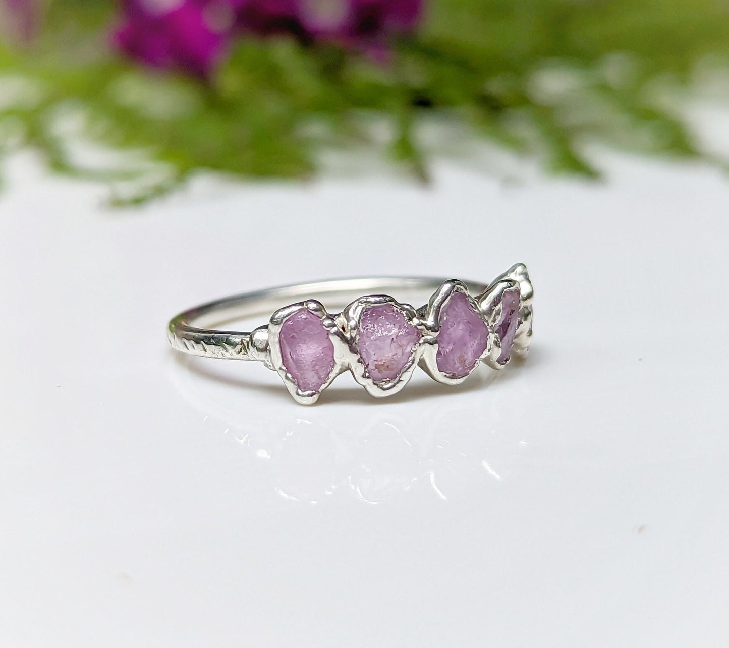 Raw pink sapphire eternity ring on handcrafted sterling silver band, featuring 5-7 small raw sapphires.