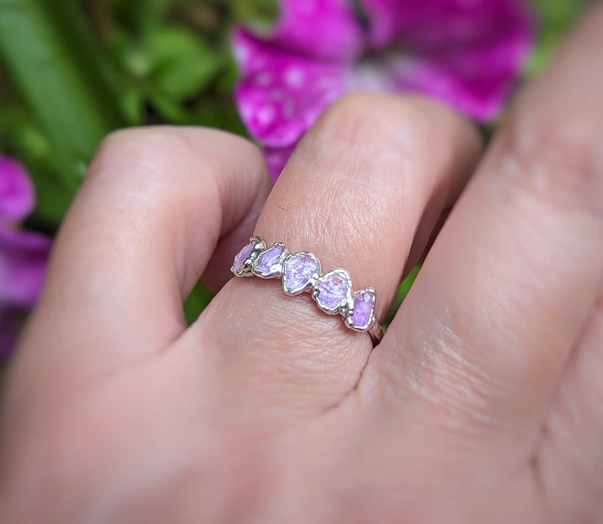 Raw pink Sapphire eternity ring on a hand, featuring 5-7 small raw sapphires set in a sterling silver band.