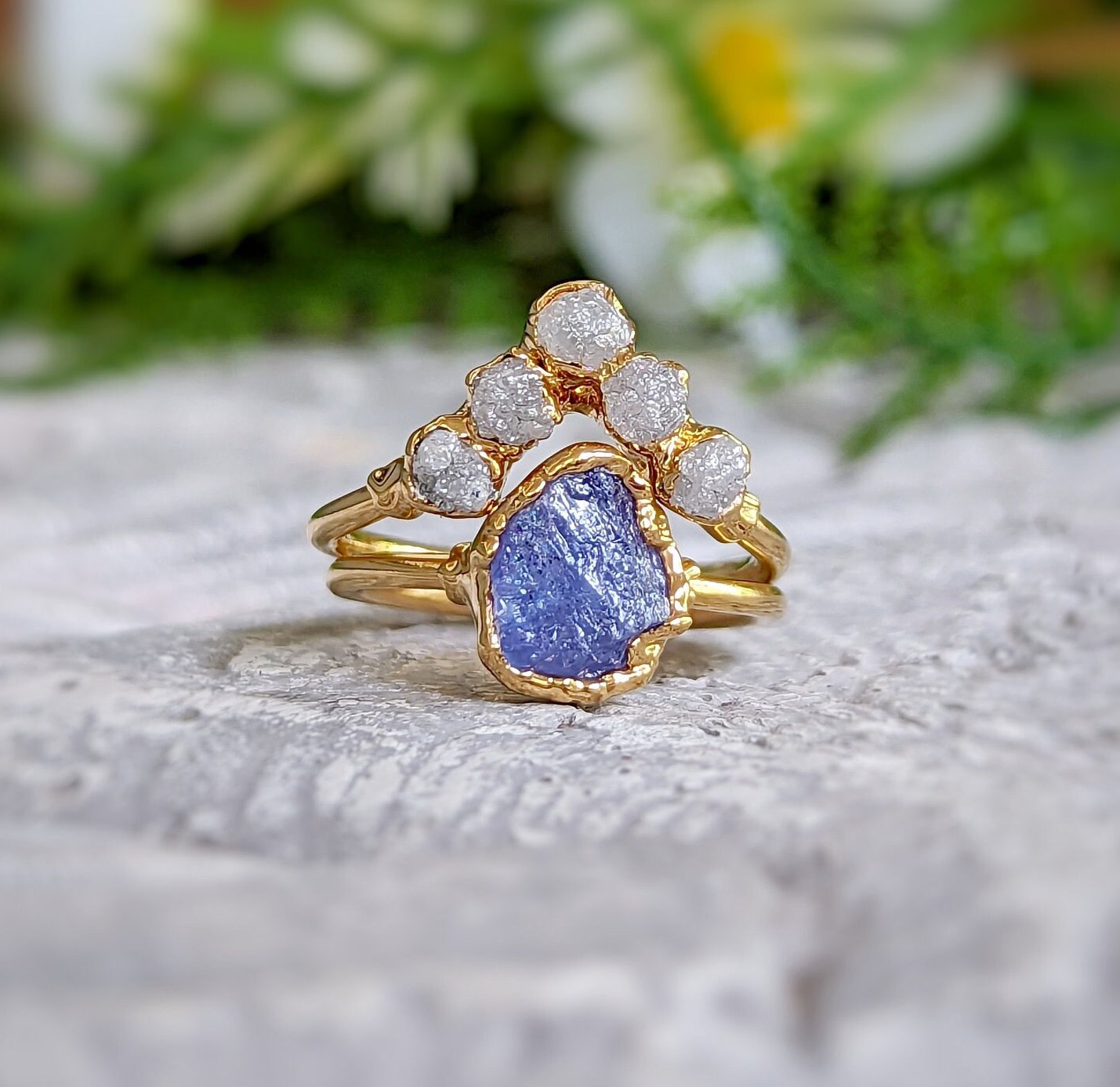 Raw Tanzanite and diamond Chevron wedding ring set on a textured surface with floral background.