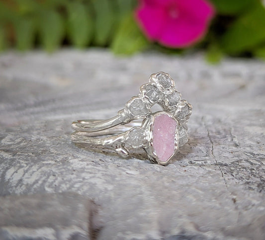 Raw pink Morganite and diamond wedding ring set on a stone surface with pink flower in background.