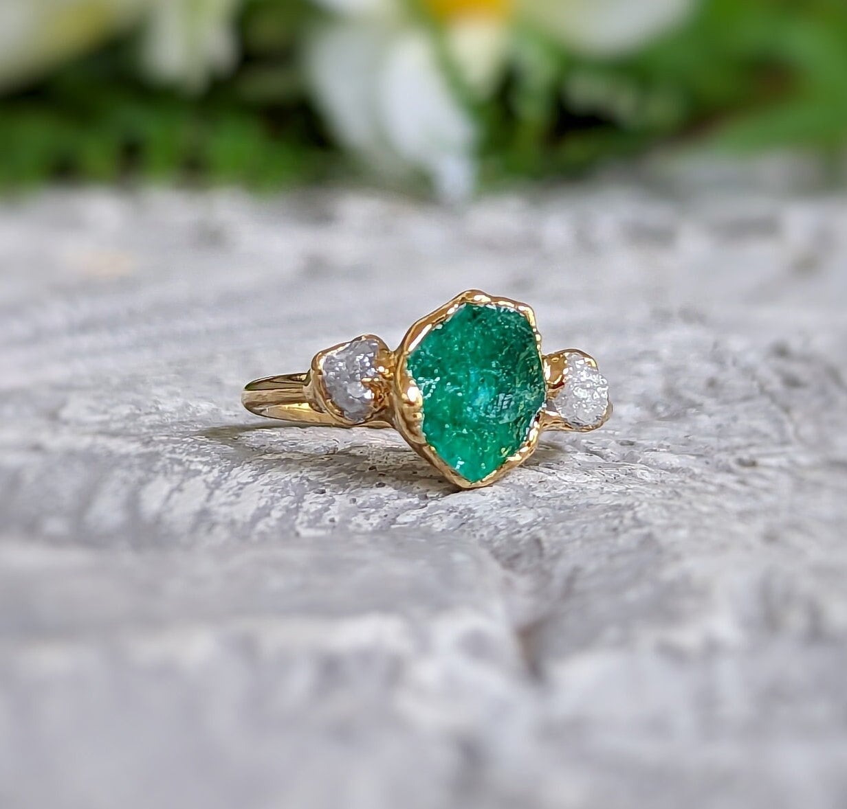 Raw emerald and diamond chevron bridal ring set on a textured surface, showcasing a unique 18k gold design.