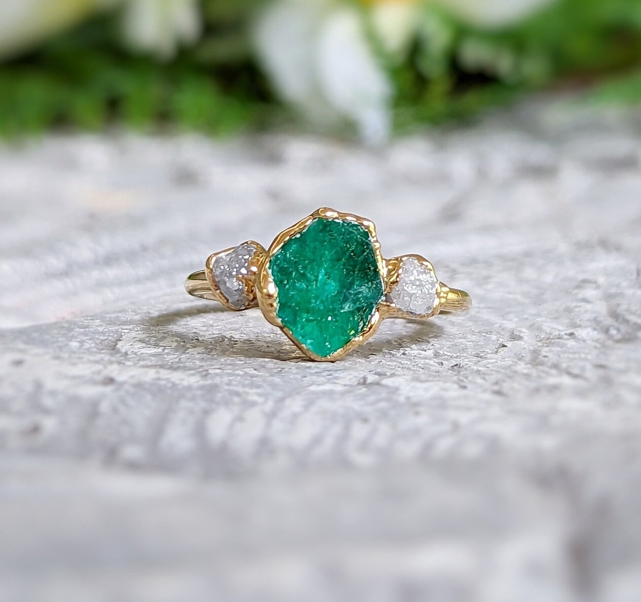 Raw emerald and diamond Chevron bridal ring set on a textured surface, showcasing unique design and elegance.