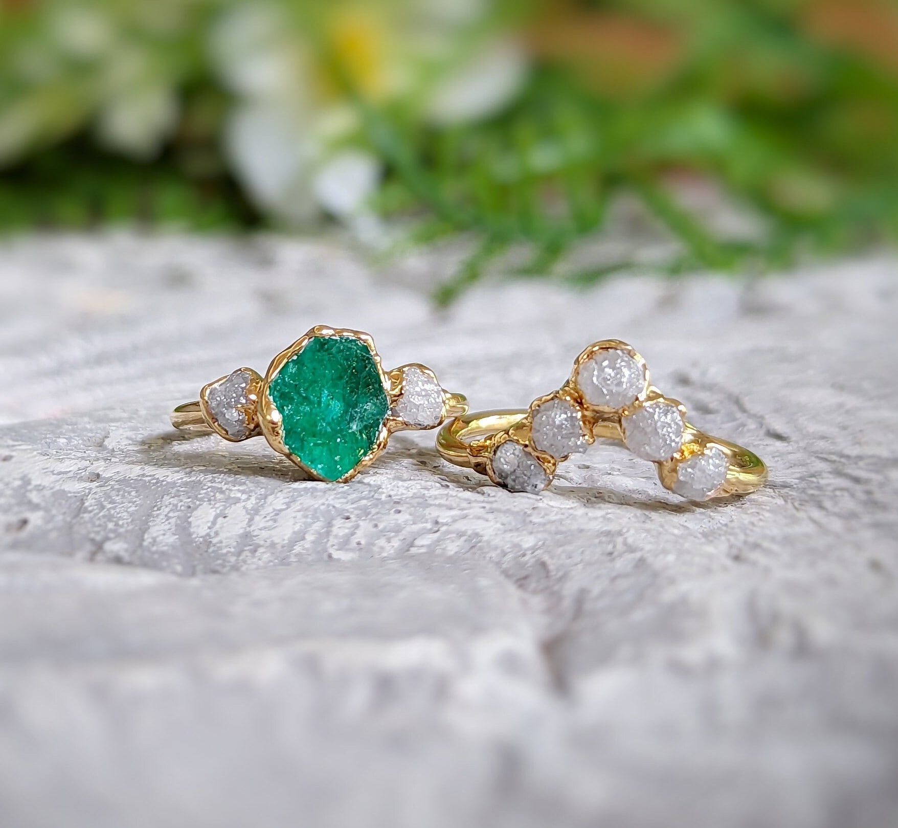 Raw emerald and diamond chevron bridal ring set on a textured surface, showcasing unique gold band design.