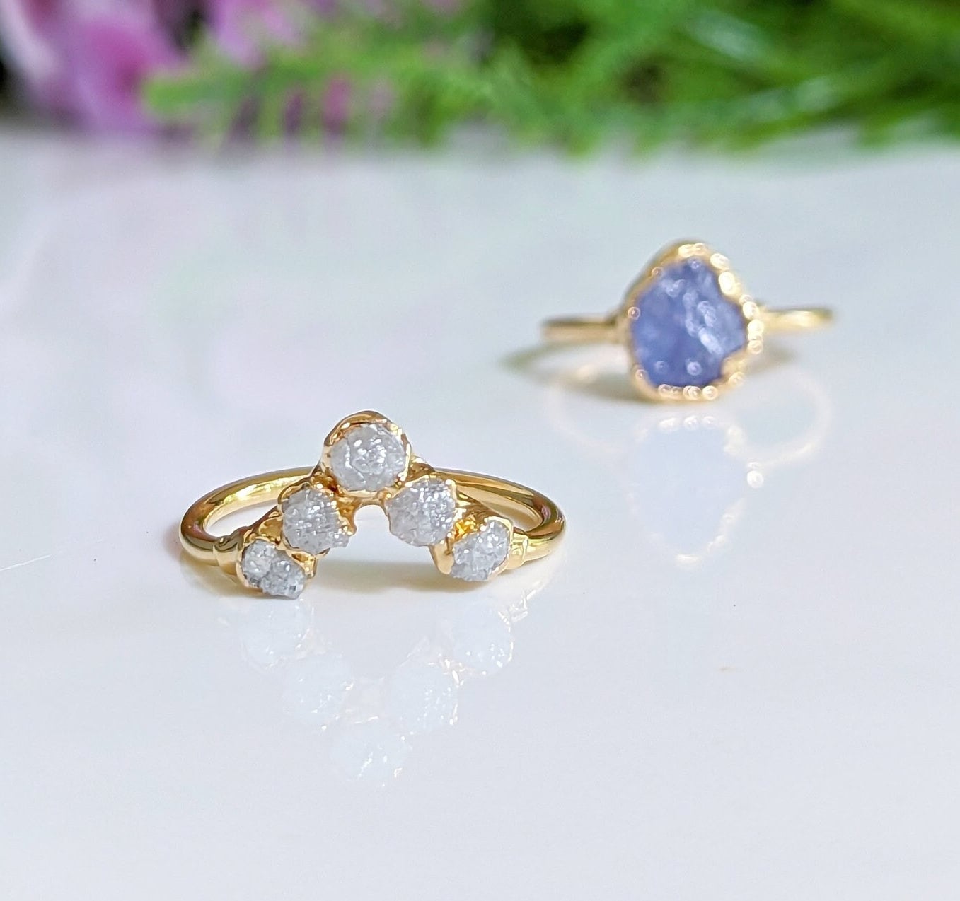 Raw Tanzanite and diamond Chevron wedding ring set on a reflective surface with a floral background.