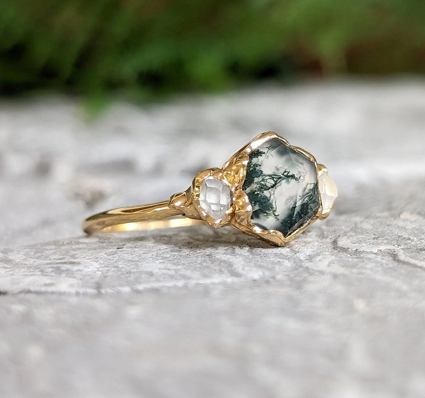 Moss Agate and Herkimer diamond engagement ring on a stone surface, showcasing hexagon shape and gold band.