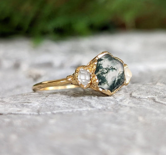 Moss Agate and Herkimer diamond engagement ring on a stone surface, showcasing hexagon shape and gold band.