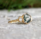 Moss Agate and Herkimer diamond engagement ring on a stone surface, showcasing hexagon shape and gold band.