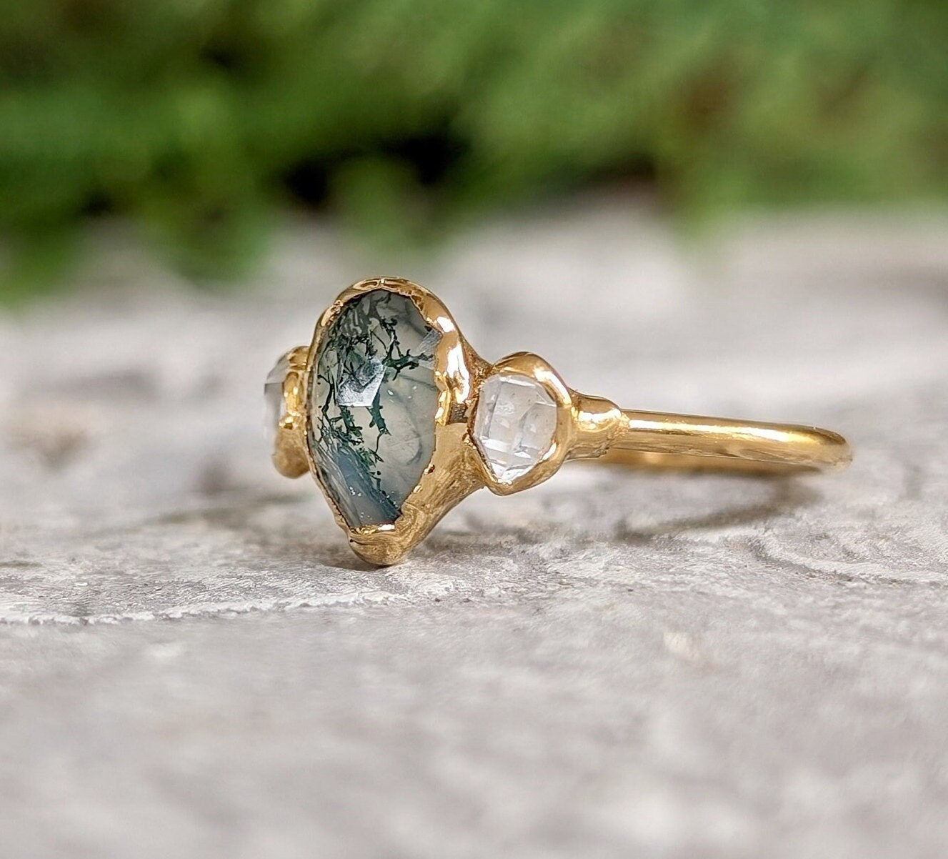 Moss Agate and Herkimer diamond engagement ring on stone background, showcasing pear shape design in 14k gold setting.