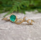 Raw Emerald and diamond Chevron wedding ring set on a textured surface, featuring gold and green hues.