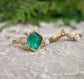 Raw emerald and rough diamond Chevron wedding ring set on a textured surface, featuring unique natural stones and 18k gold.