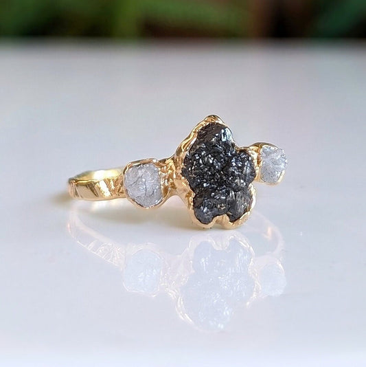 Raw uncut Black Diamond engagement ring on a gold band featuring two smaller raw diamonds.