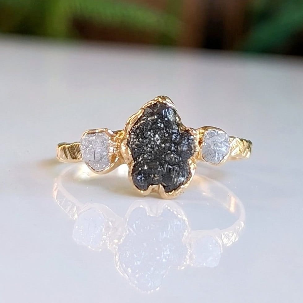 Raw black diamond engagement ring with rough uncut black diamond and two smaller raw diamonds on a gold band.