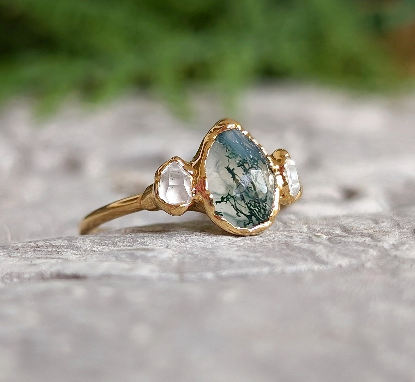 Moss Agate and Herkimer diamond engagement ring on a stone surface, featuring a pear-shaped Moss Agate and 14k gold band.