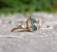 Moss Agate and Herkimer diamond engagement ring on a stone surface, featuring a pear-shaped Moss Agate and 14k gold band.